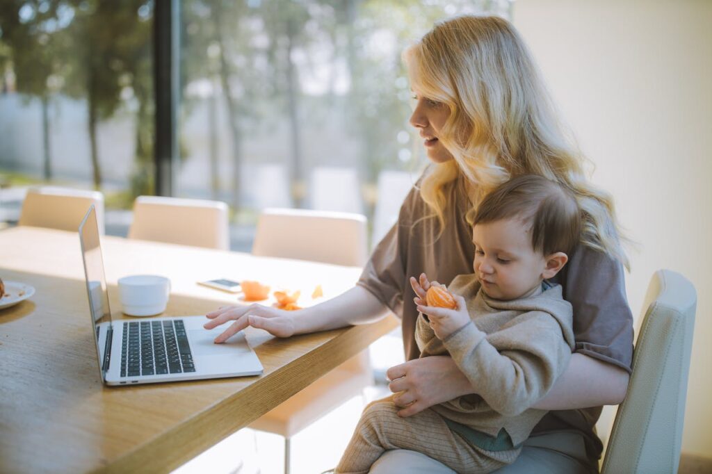 pexels-photo-4079281 A mother works on a laptop at home while holding her baby, showcasing remote working and parenting.